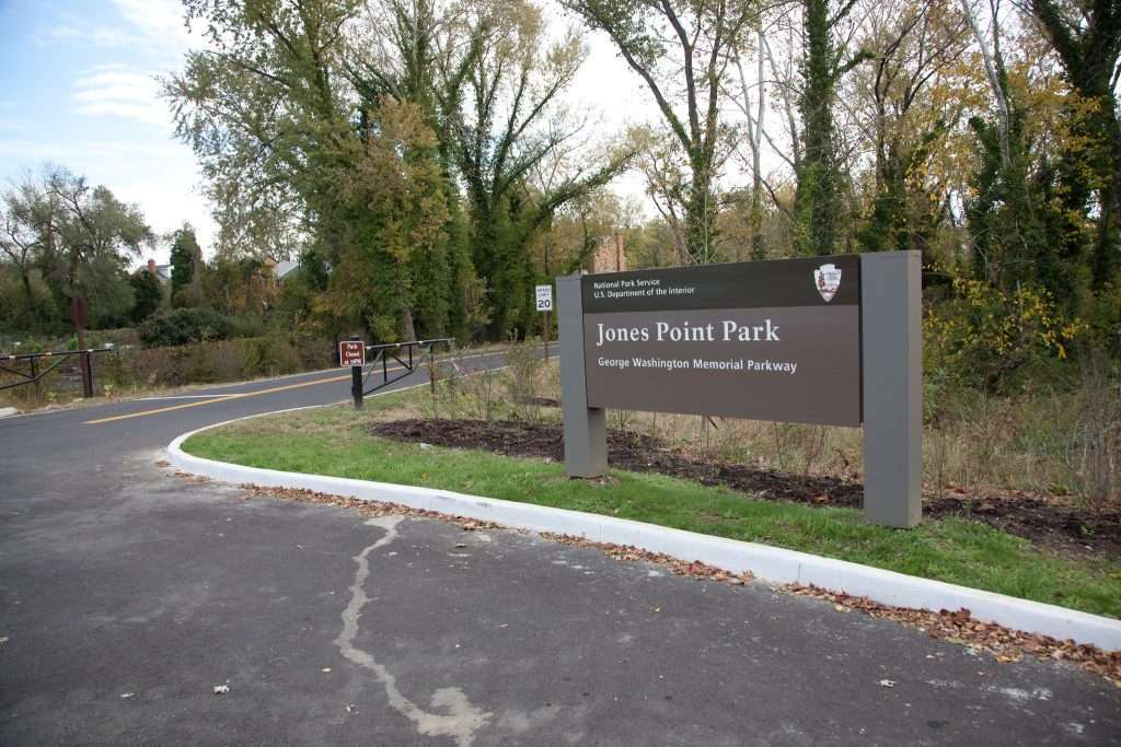 Arlington VA 20 Jones Point Park entrance sign along George Washington Memorial Parkway with paved road, autumn trees, and National Park Service branding in Alexandria