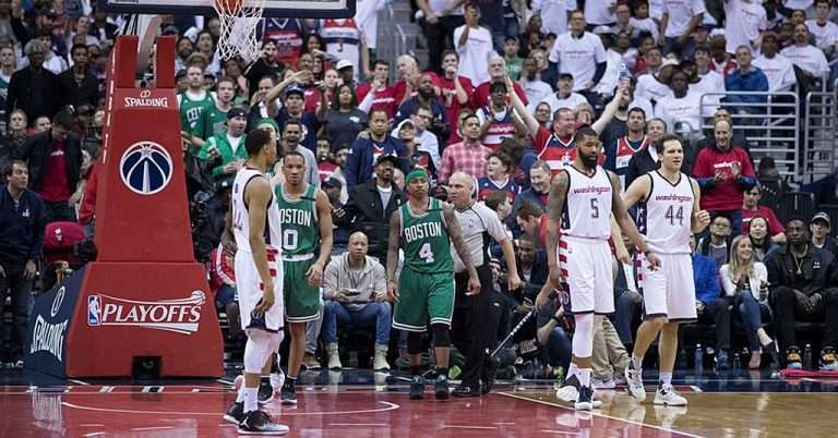 Arlington VA 27 Washington Wizards players face off against Boston Celtics players during an NBA playoff game, with a packed arena of fans in the background cheering and watching intensely.