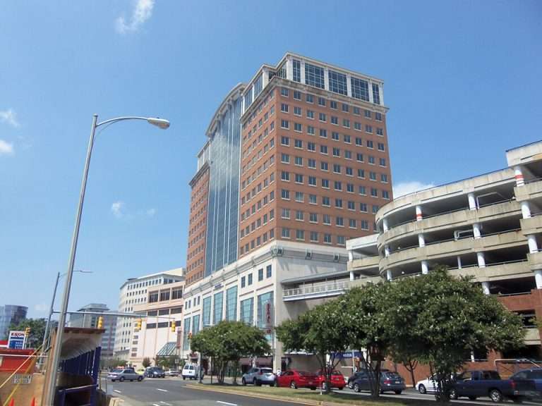 Arlington VA 17 Tall red-brick building with glass windows, adjacent to a circular parking structure under a clear blue sky.