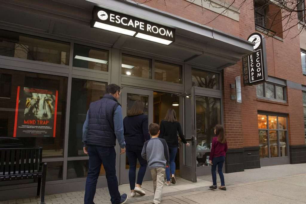 Arlington VA 16 People entering an escape room venue with a sign above and a "Mind Trap" poster on the window.