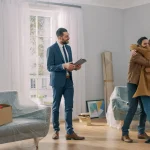 Happy couple are hugging in a home they have just purchased in Washington DC with the Nomadic real estate agent looking over in joy.