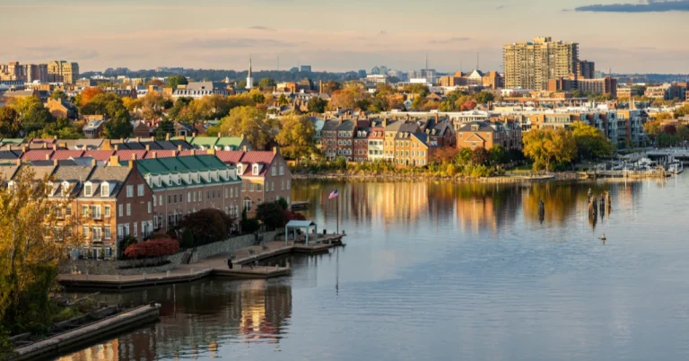 Scenic view of waterfront homes and historic architecture in Old Town Alexandria, Virginia, with calm river reflections and fall foliage.