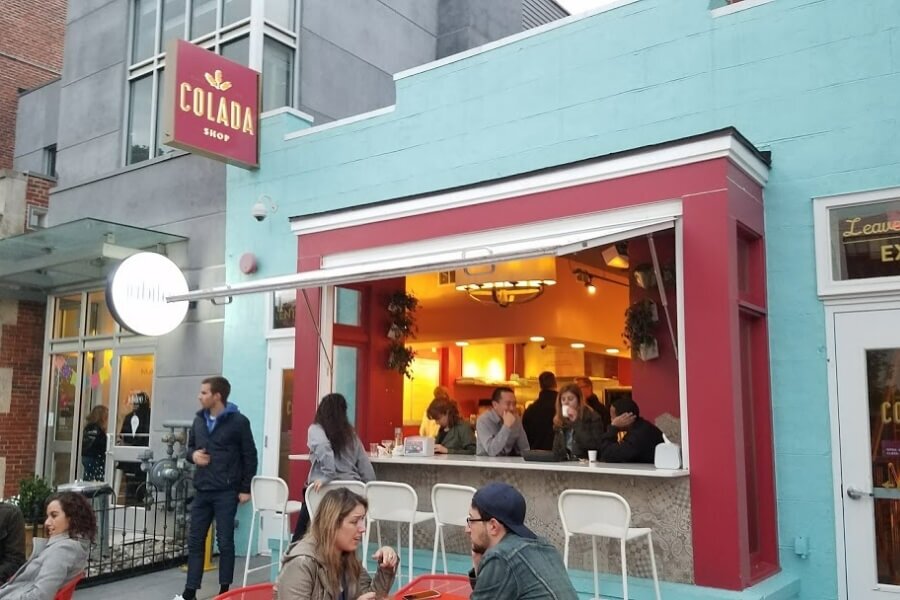 colorful storefront of Colada Shop with outdoor seating and window seating.